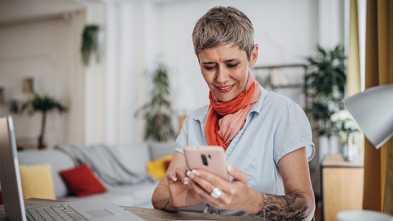 Mature woman sitting at desk at home with phone